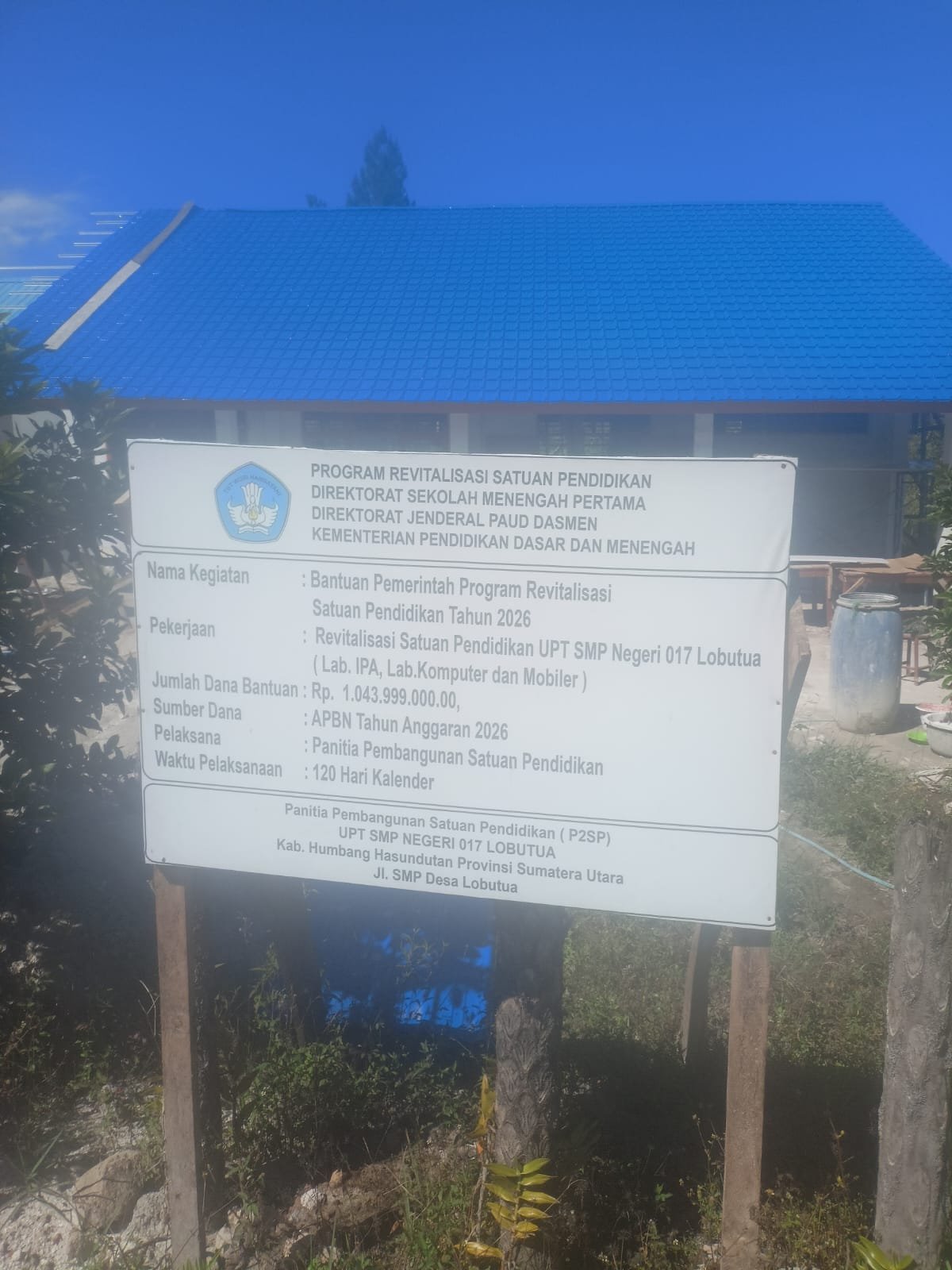 Papan informasi proyek revitalisasi di UPT SMP Negeri 017 Lobutua, Kabupaten Humbang Hasundutan. Proyek senilai Rp1.043.999.000 yang bersumber dari APBN Tahun Anggaran 2026 itu dikerjakan selama 120 hari kalender oleh Panitia Pembangunan Satuan Pendidikan. Foto: http://Instrumentasi.com